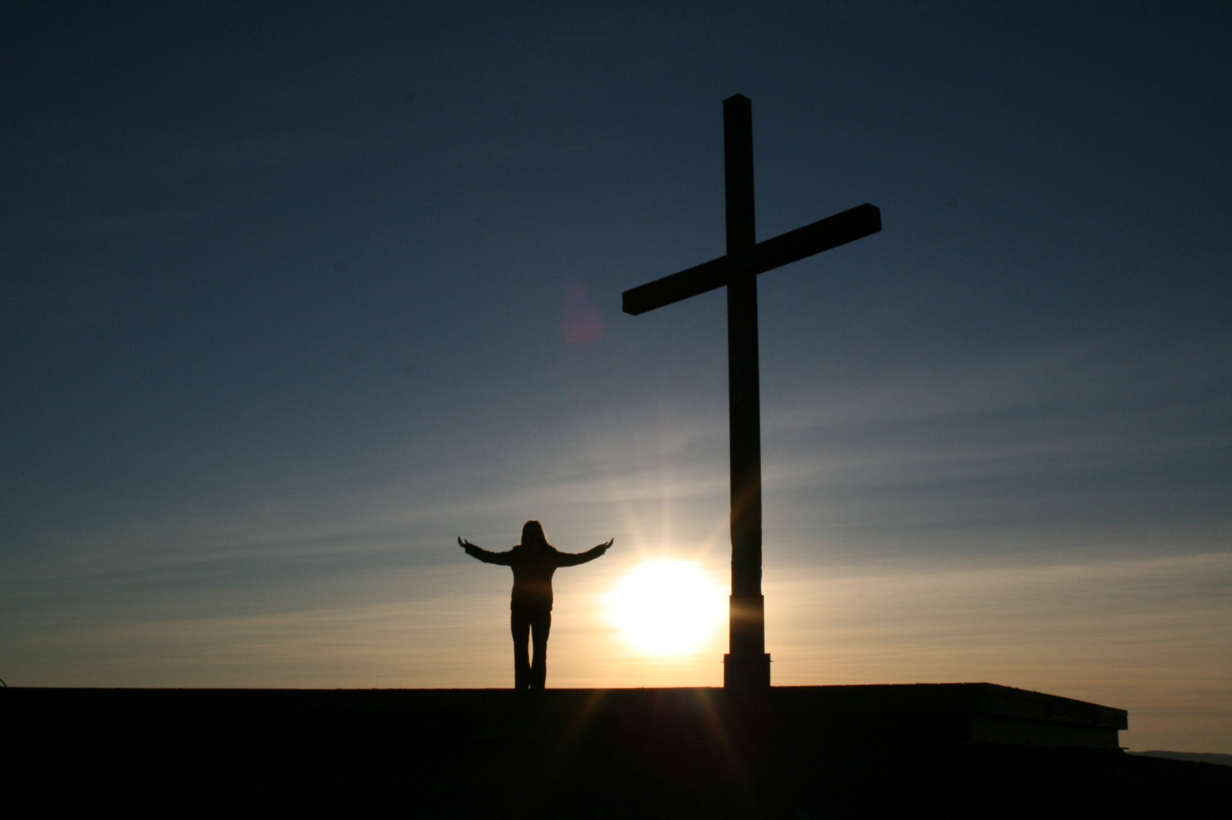 Silhouette of a Person Standing Near a Cross